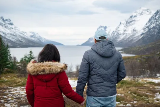 Two guests holding hands while looking out over a fjord