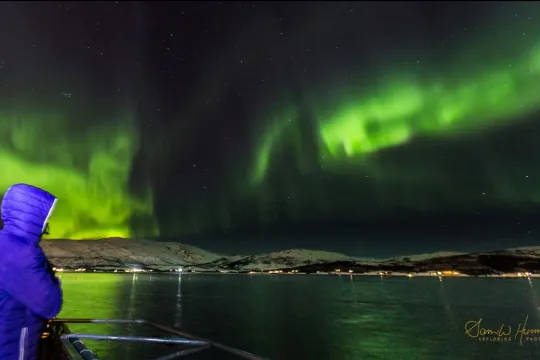 En gjest ser nordlyset danse over fjorden under en båttur i Tromsø.