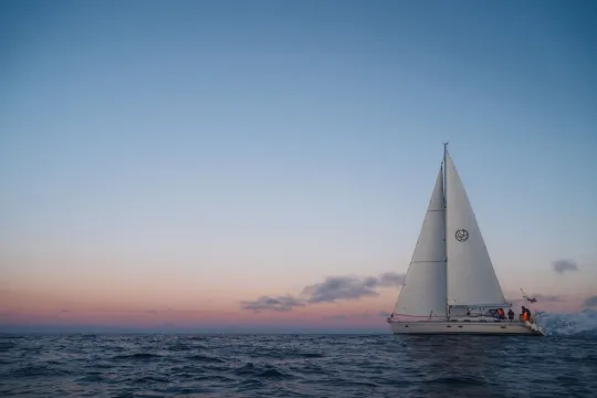 Seilbåt fra SailNorge på havet i Nord-Norge, omgitt av arktisk kystlandskap og vakre farger på kveldshimmelen.