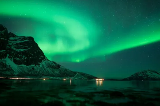 Grønt nordlys lyser opp nattehimmelen over en fjord omgitt av snødekte fjell. Et vakkert nordlyslandskap i Tromsø-regionen i Nord-Norge.