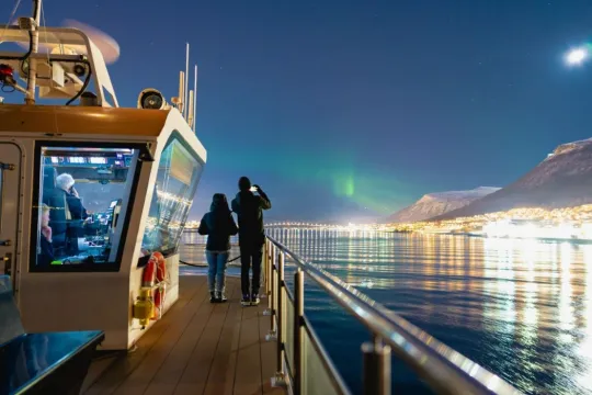 Guests watch the green Northern Lights above the Arctic fjords from the deck of Brim Explorer's boat during an evening dinner cruise from Tromsø.