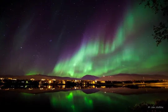 Northern lights over the water and city lights