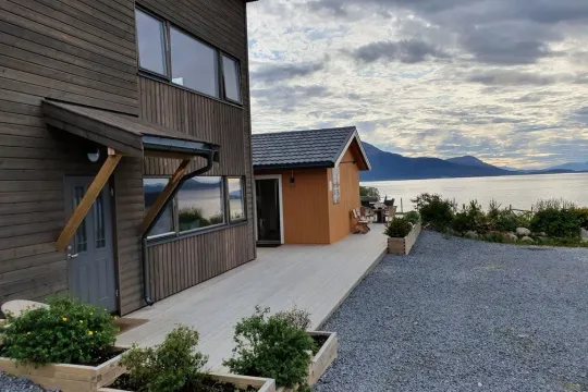 Trehus ved vann med fjell i bakgrunnen og hage foran