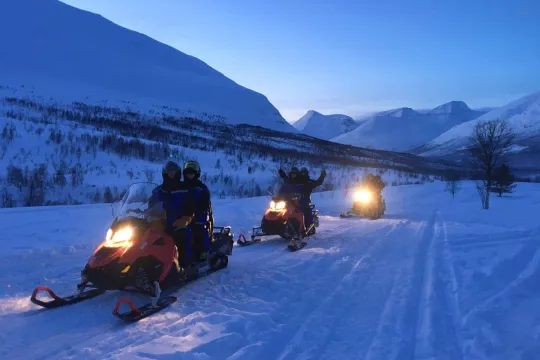 Snow scooters drive in a line through the mountains