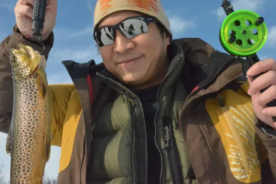 A happy guest shows off their catch during an ice fishing trip in the Tromsø region. Discover traditional ice fishing and winter activities in Northern Norway.