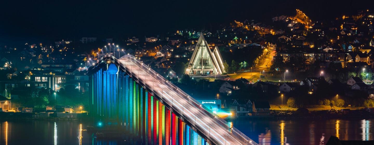 The Tromsø bridge lit up in colours, with the Arctic Cathedral in the background