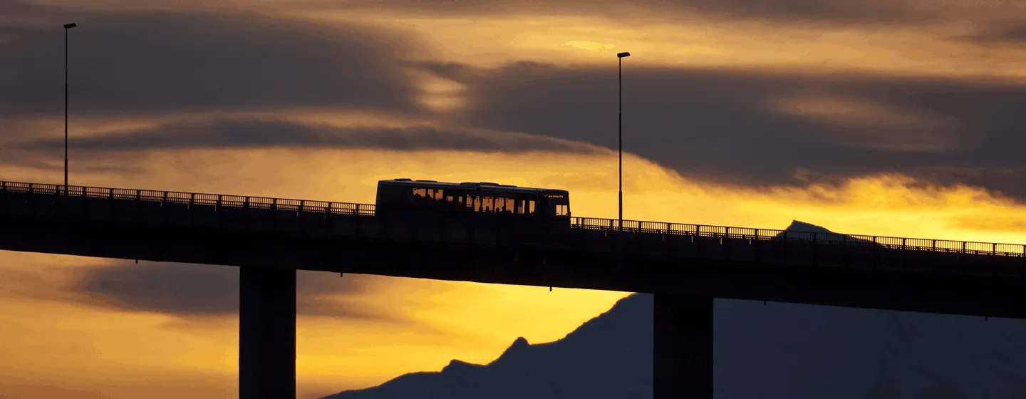 Bus driving over bridge with orange sky backdrop