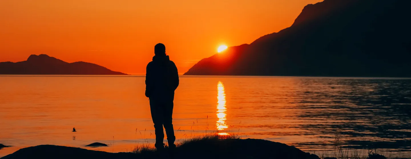 Person nyter utsikten og midnattssola