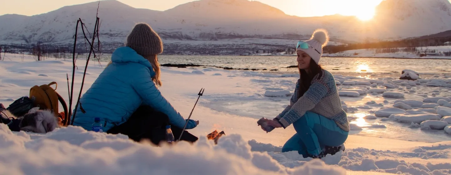 Venninner hygger seg utendørs i vinterlandskap ved havet i Tromsøregionen