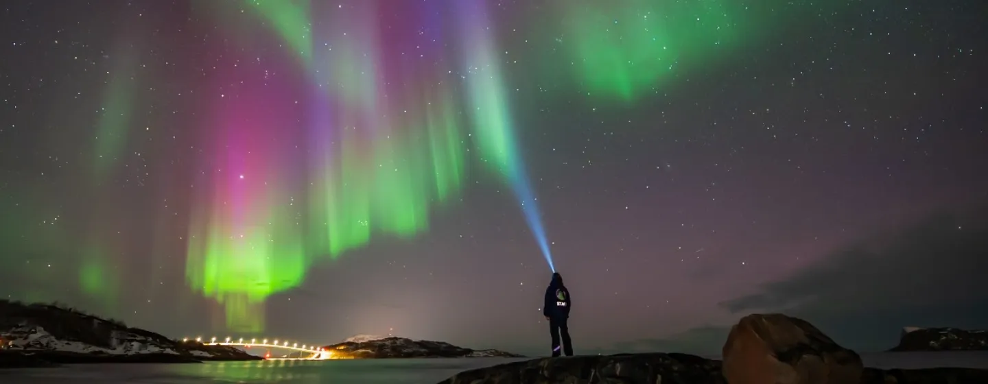 Person som ser på Nordlyset med hodelykt