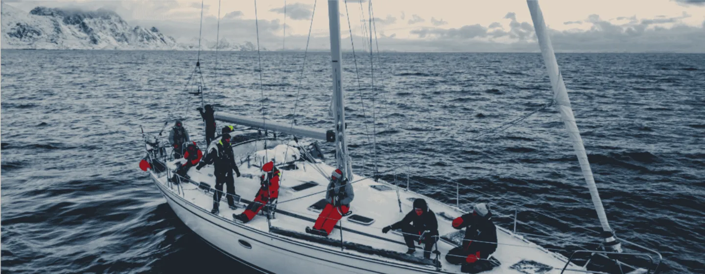 A sailboat in the arctic fjords with snow covered mountains behind