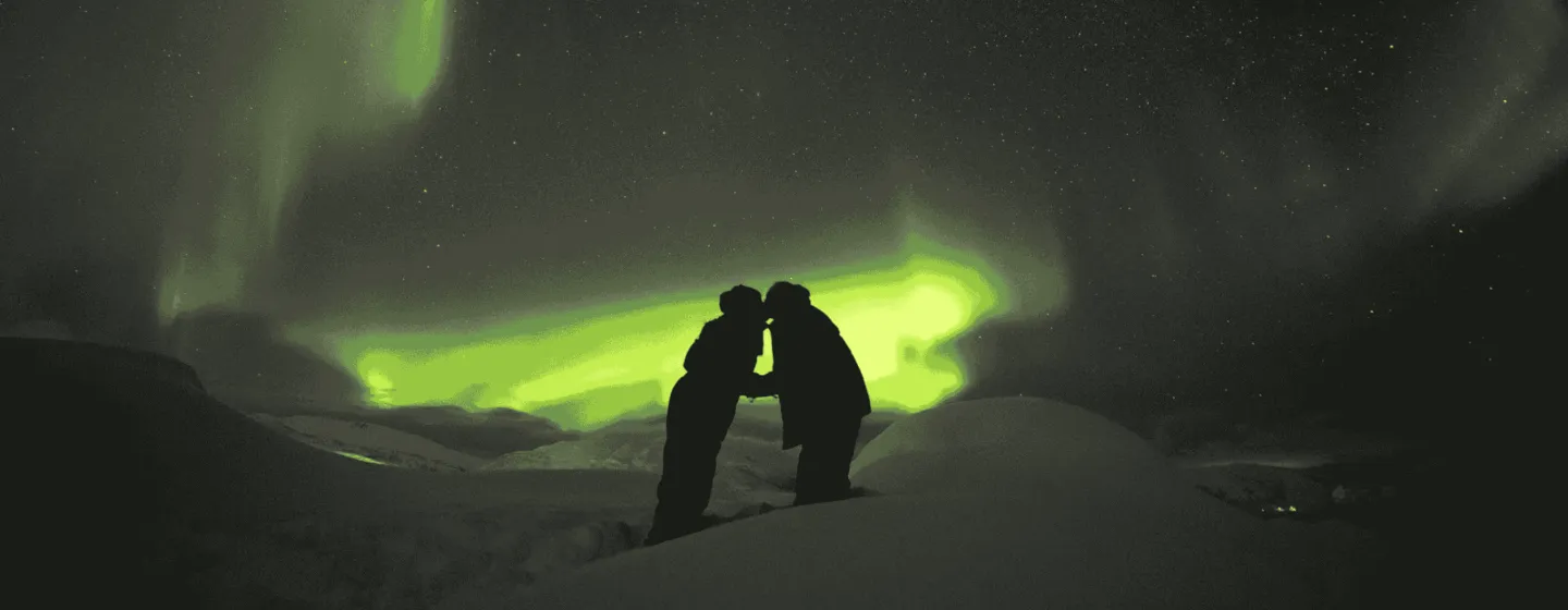 Two people under the Northern Lights in snow covered landscape