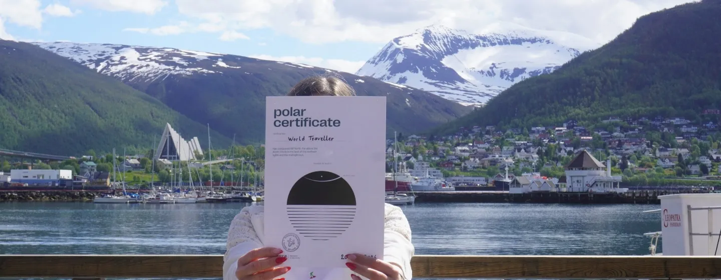 Woman holding a Polar Certificate from Visit Tromsø-Region in the summer with the Arctic Cathedral and Tromsdalstinden in the background.