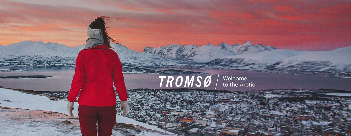 Woman hiking with a view of Tromsø during sunset with Visit Tromsø logo
