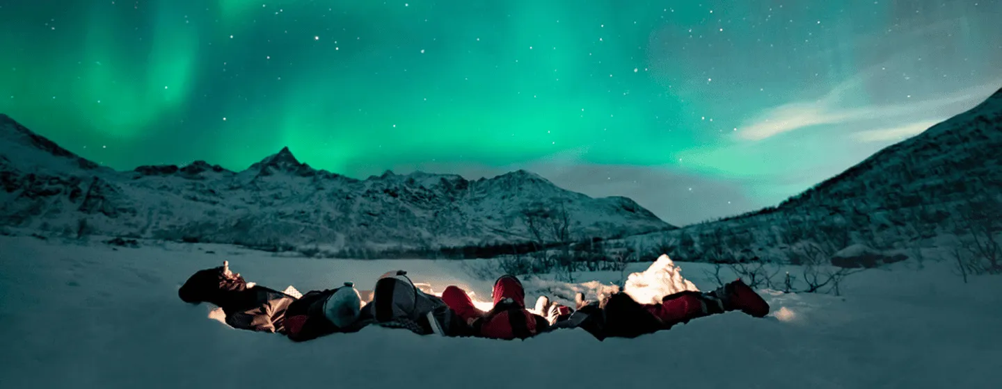 Gjester som ligger ved et bål og ser på nordlyset