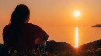 Woman sitting in nature and enjoying the midnight sun in the Tromsø region.